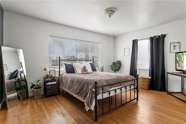 a bedroom with a bed next to a window with wooden floor