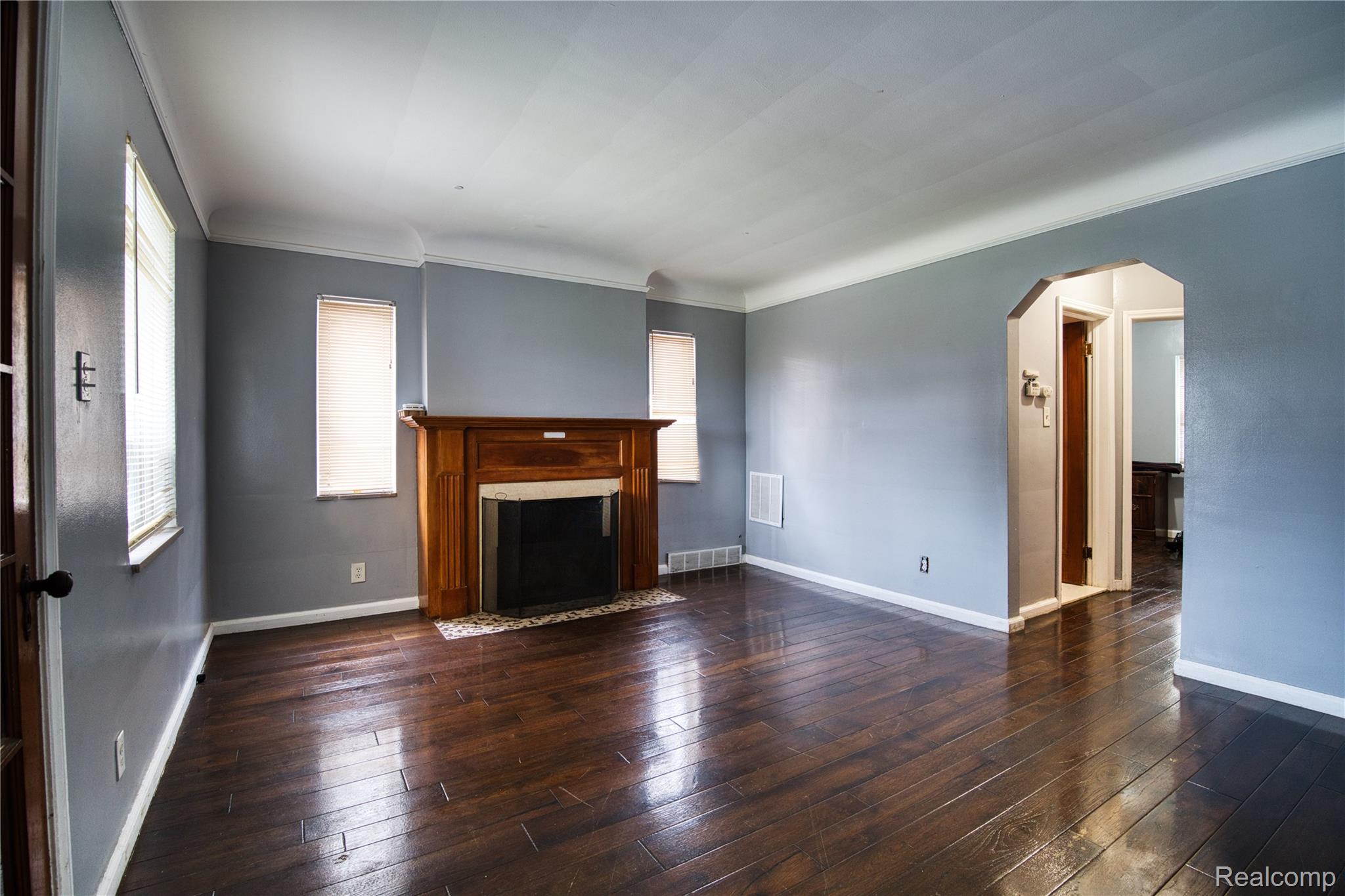 13644 Castleton Street Detroit, MI 48227 - Photo 2 of 18 Wood-finish flooring, classic wooden fireplace mantel, arched doorway, multiple windows, and crown molding
