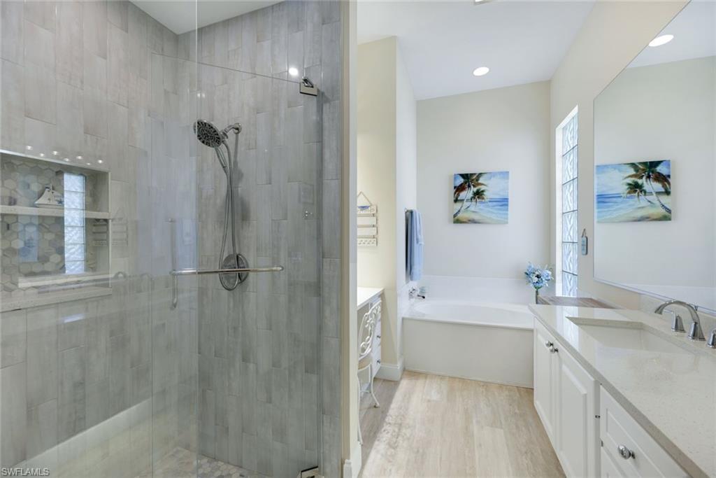 3108 Dominica Way Naples, FL 34119 - Photo 13 of 39 Upgraded shower with glass enclosure, light-toned wood-finish flooring, built-in tub, dual vanity with undermount sinks, and a privacy window featuring glass blocks