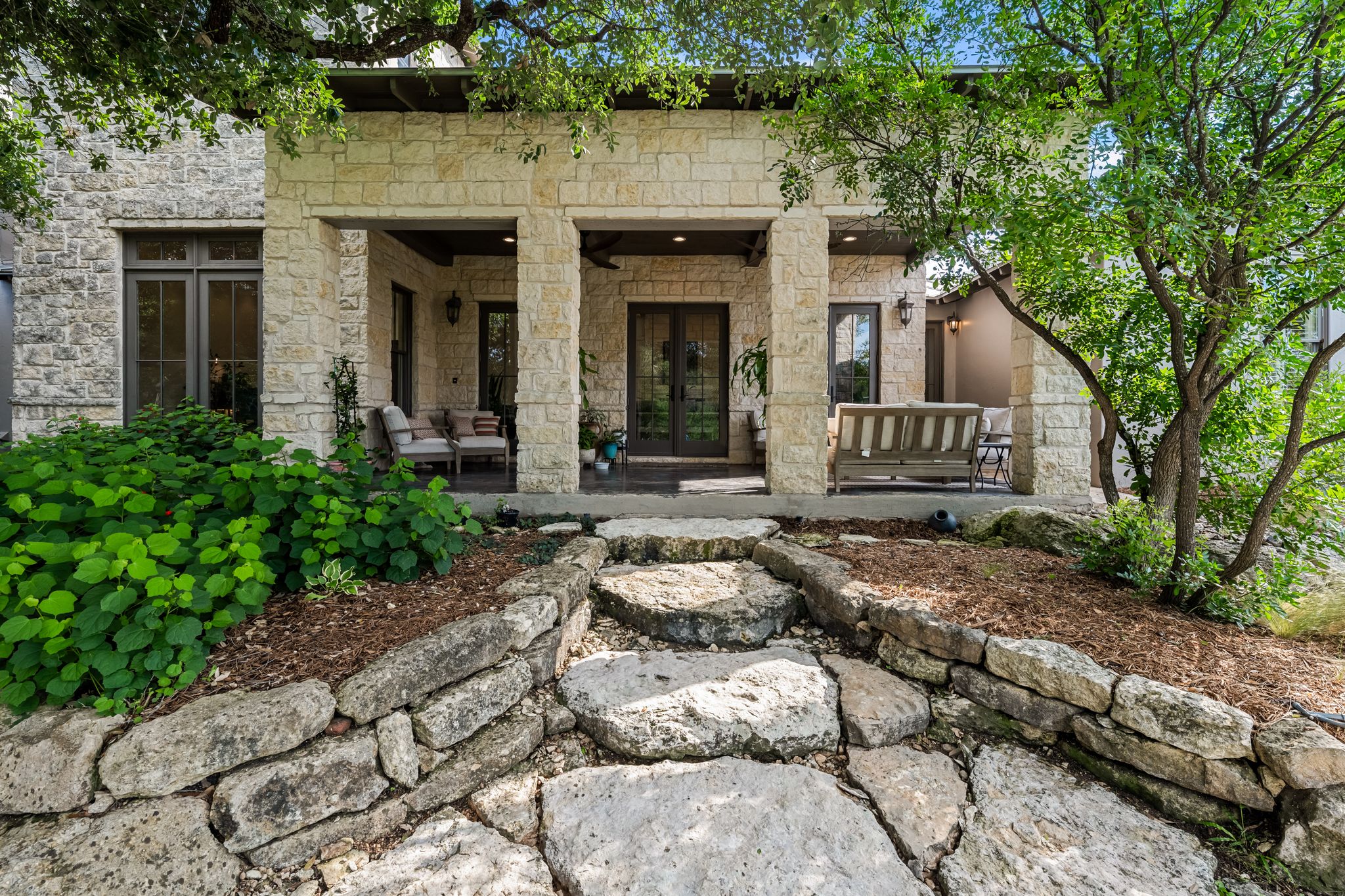 195 Desert Flower Spring Branch, TX 78070 - Photo 5 of 40 Stone façade home featuring a covered front porch, stone retaining walls, stone step pathway, and mature trees