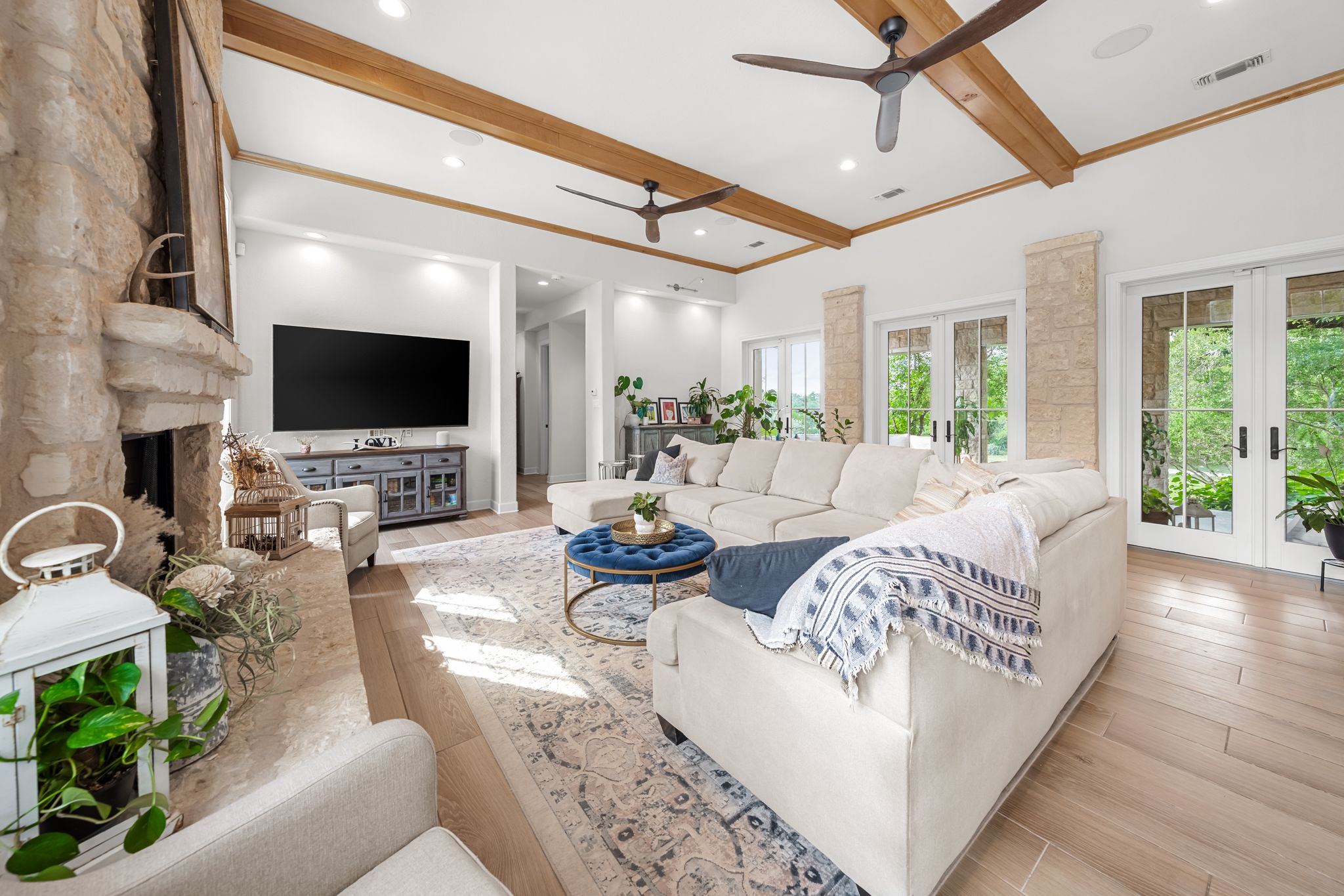 195 Desert Flower Spring Branch, TX 78070 - Photo 8 of 40 Spacious living area featuring a stone fireplace, wood-finish flooring, exposed ceiling beams, and multiple ceiling fans