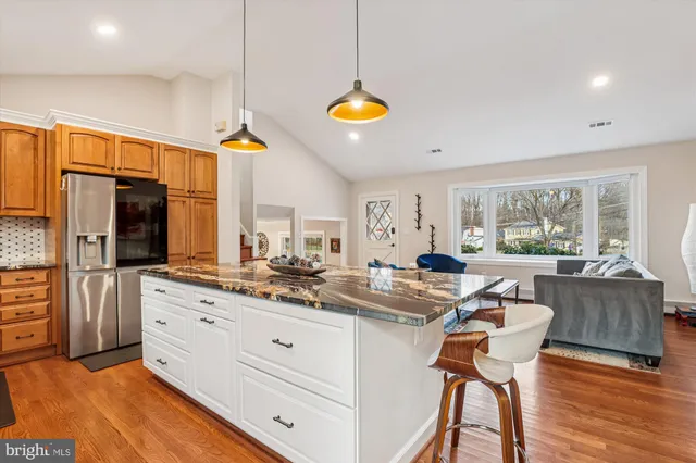 a kitchen with stainless steel appliances kitchen island granite countertop a stove a refrigerator and white cabinets with wooden floors