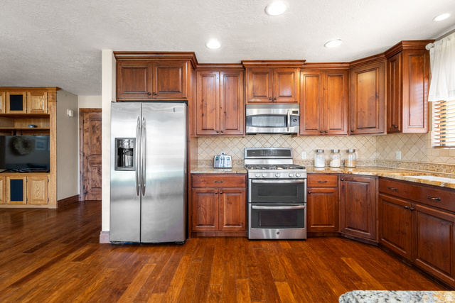 892 Cambridge Drive St. George, UT 84770 - Photo 27 of 65 Kitchen featuring rich wood cabinetry, stainless steel appliances, patterned tile backsplash, and stone countertops