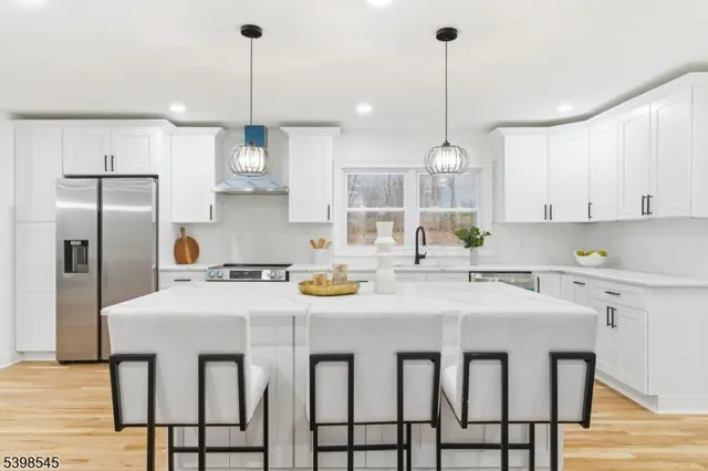 a kitchen with stainless steel appliances granite countertop a sink a stove a refrigerator and white cabinets with wooden floor