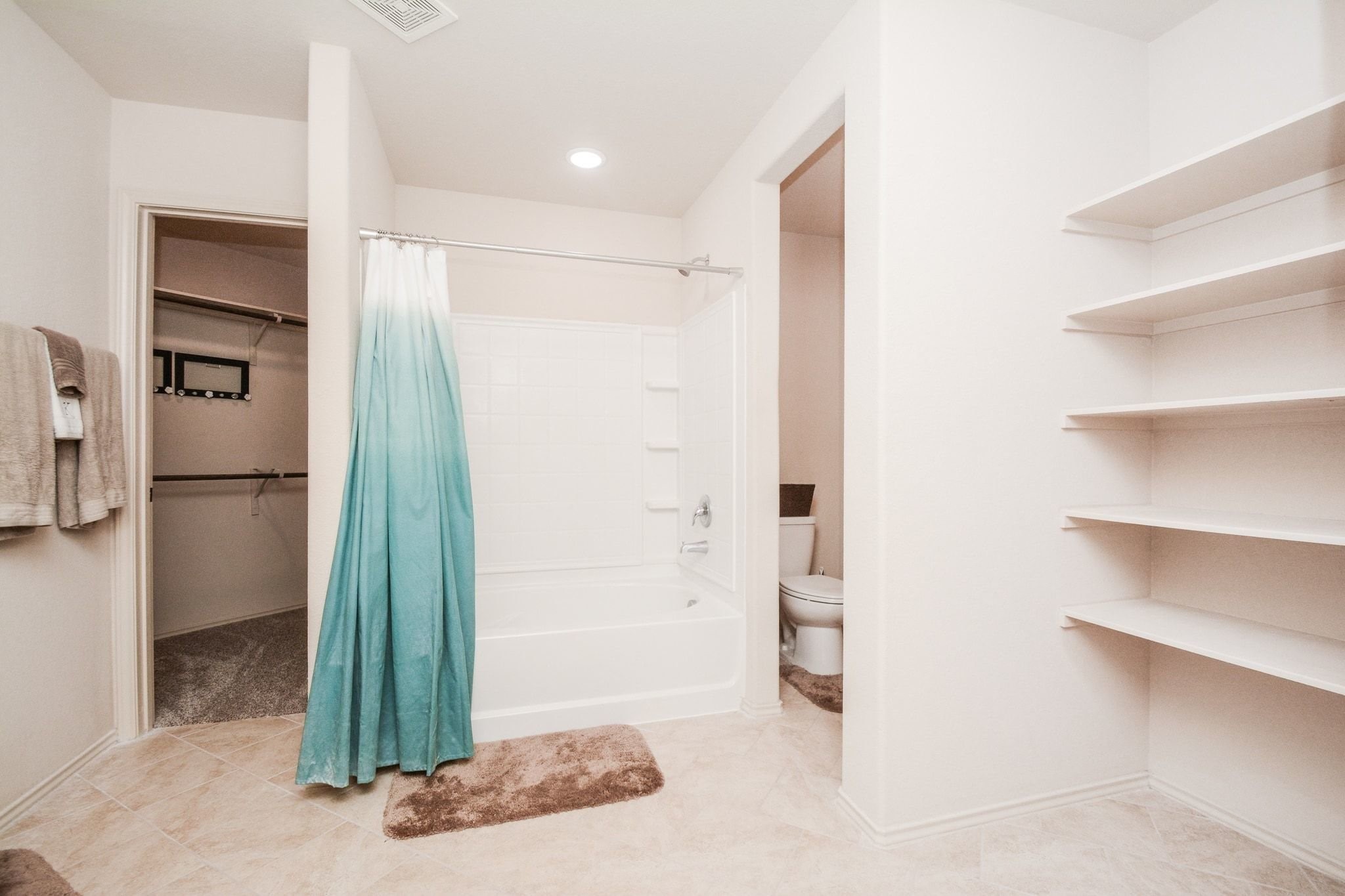 23318 Dukes Run Drive Spring, TX 77373 - Photo 28 of 41 This bathroom features a tub with a shower, neutral tiles, built-in shelving, and access to a walk-in closet. The space is well-lit and offers a clean, minimalist design.