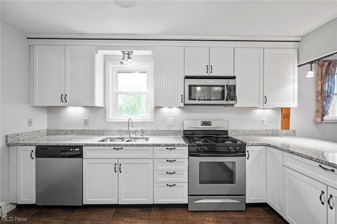 228 Cavalry Road Vermilion, OH 44089 - Photo 14 of 34 Kitchen featuring light stone counters, appliances with stainless steel finishes, dark tile flooring, and white cabinetry