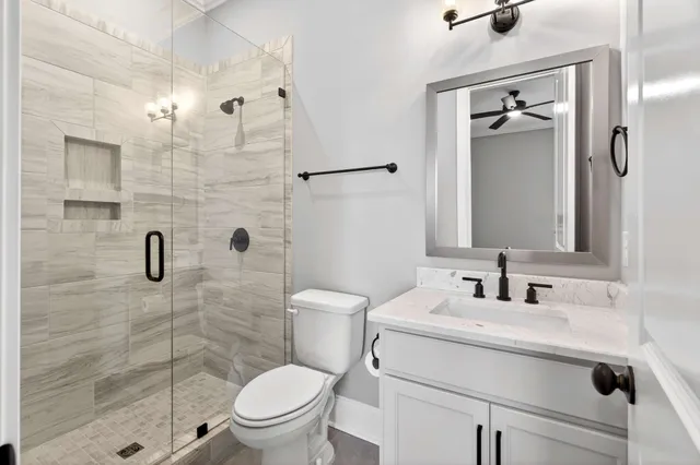 a bathroom with a granite countertop sink a toilet a mirror and shower