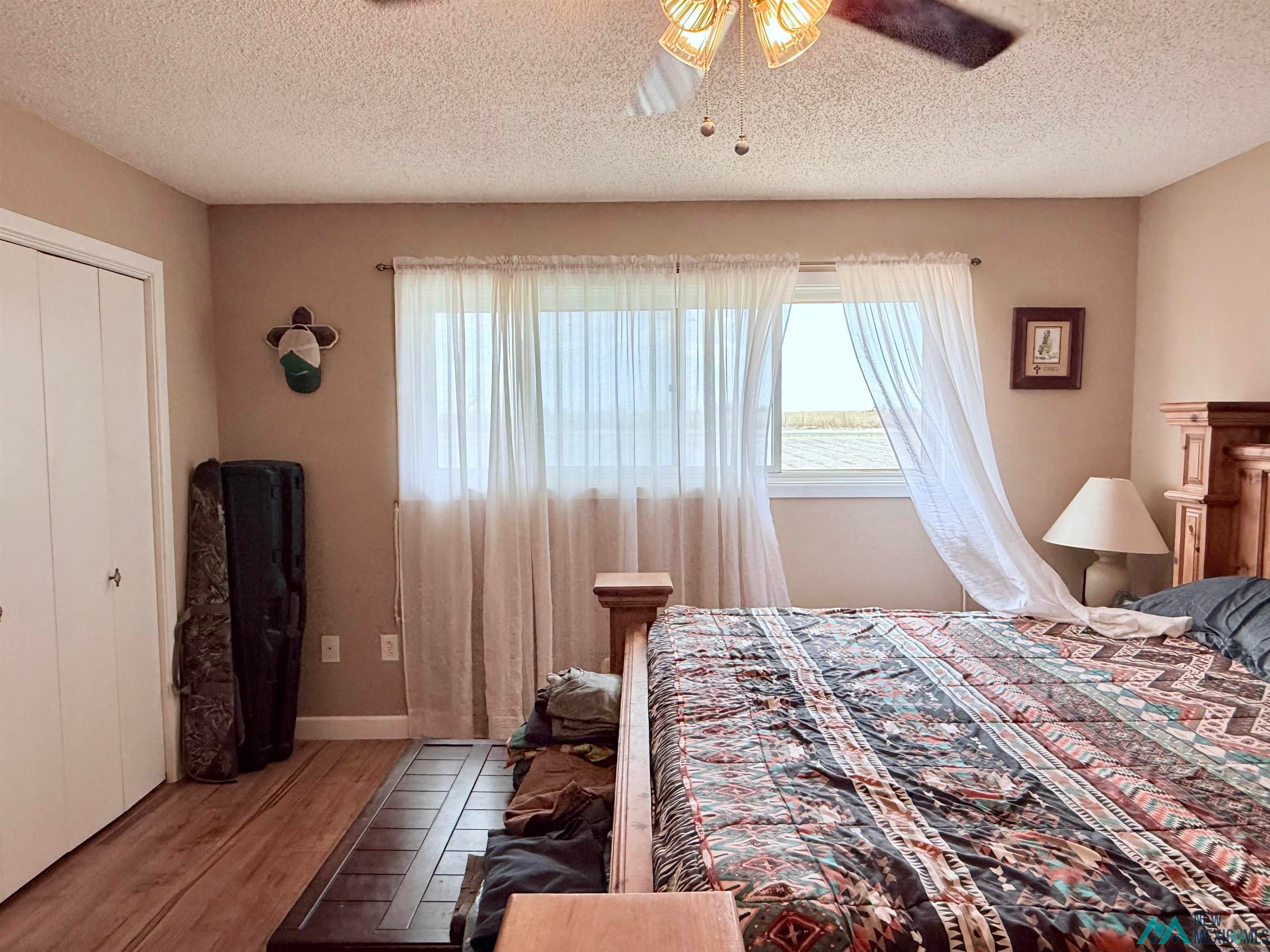 997 State Rte 108 Texico, NM 88135 - Photo 20 of 33 Bedroom featuring wood-finish flooring, a window with sheer curtains, a ceiling fan with integrated lighting, and white bi-fold closet doors