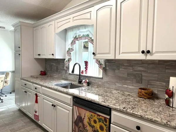 a kitchen with granite countertop a sink stainless steel appliances white cabinets and a window