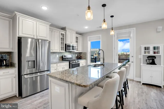 a kitchen with stainless steel appliances granite countertop a refrigerator a sink dishwasher a stove and white cabinets with wooden floor