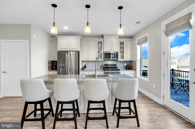 a kitchen with stainless steel appliances kitchen island granite countertop a dining table chairs and a refrigerator