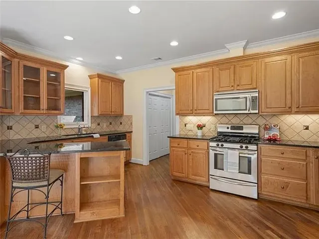 a kitchen with stainless steel appliances granite countertop a stove a sink dishwasher a microwave oven and a refrigerator with wooden floor