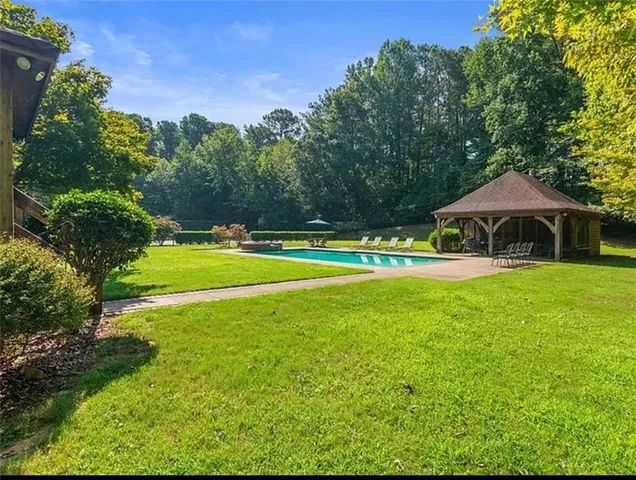 a view of pool with lawn chairs and large trees