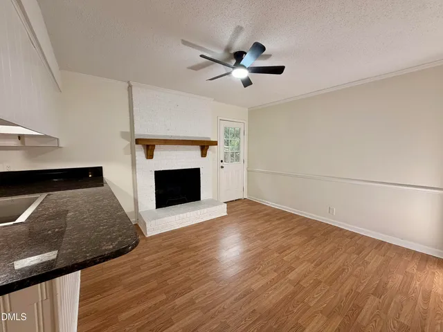 a view of a livingroom with a fireplace a ceiling fan and wooden floor