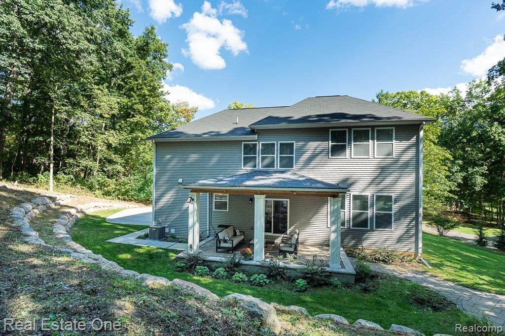 201 Beechview Drive Rochester, MI 48306 - Photo 43 of 49 Exterior siding with multiple windows, covered patio with white pillars, stone retaining wall, and verdant landscaping