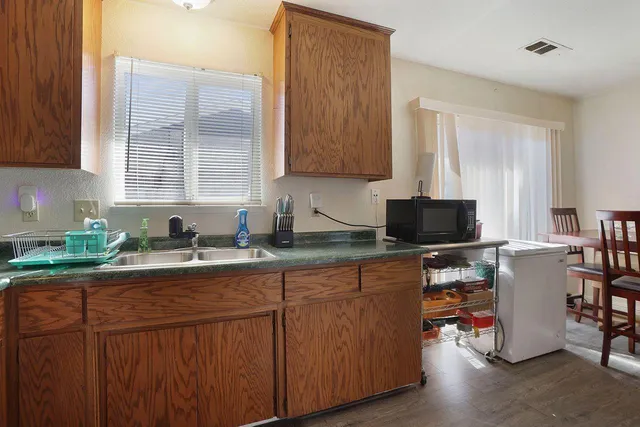 a kitchen with stainless steel appliances granite countertop wooden cabinets a sink a stove a dining table and chairs