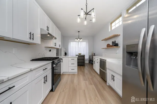 a large kitchen with stainless steel appliances a refrigerator a sink dishwasher a stove and white cabinets with wooden floor