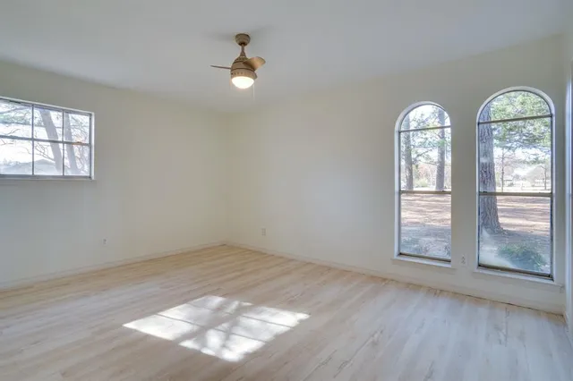 an empty room with wooden floor fan and windows