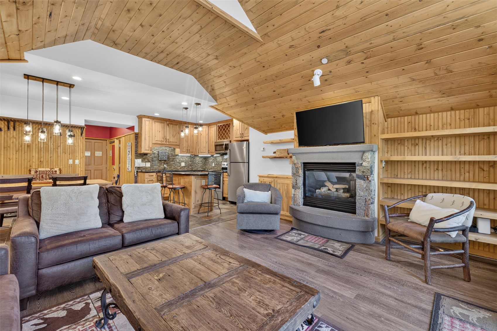 129 River Run Road, Unit 8051 Keystone, CO 80435 - Photo 8 of 50 Vaulted wood-paneled ceiling, stone-surround fireplace, built-in shelving, wood-finish flooring, and wood cabinetry