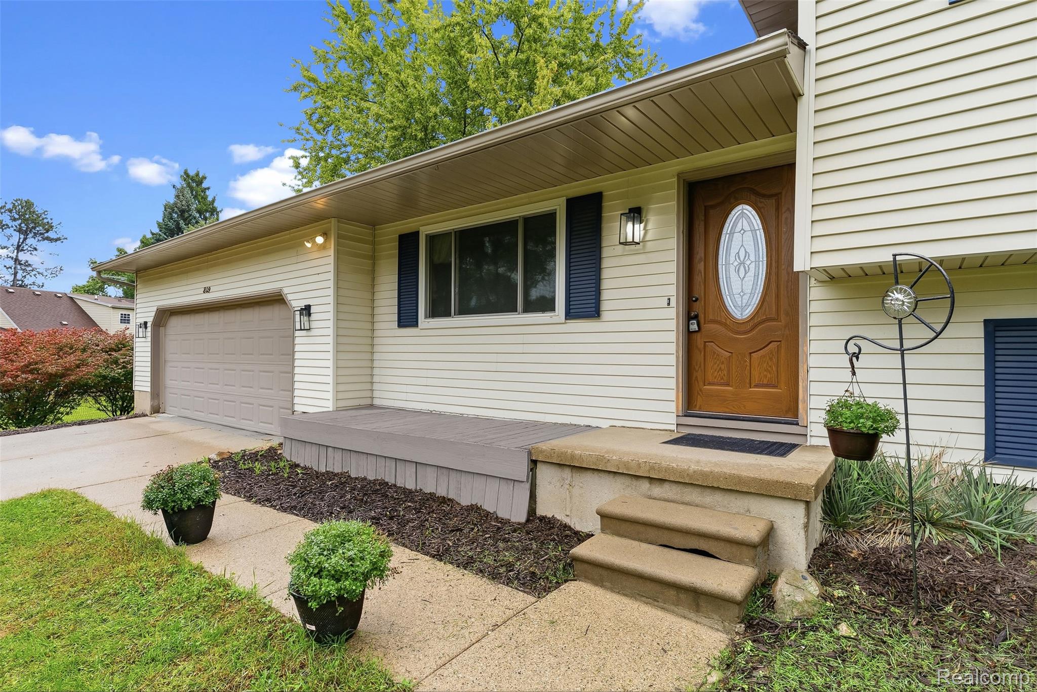 819 Alpine Trail Fenton, MI 48430 - Photo 4 of 41 Light-colored siding exterior with dark blue window shutters, attached garage, and a wood-finish entry door with an oval-shaped glass insert