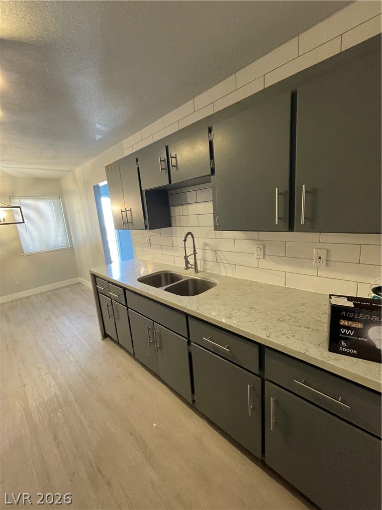 466 East Sunset Road, Unit D Henderson, NV 89011 - Photo 13 of 20 Kitchen with light stone counters, a textured ceiling, light wood finished floors, tasteful backsplash, and gray cabinets