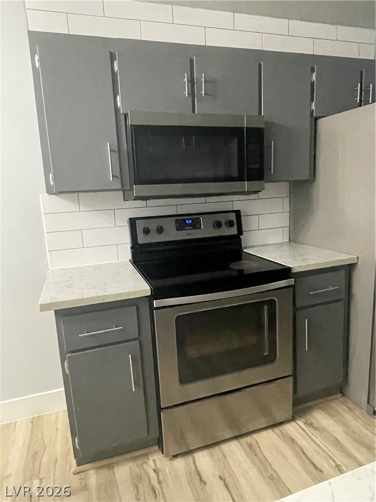 466 East Sunset Road, Unit D Henderson, NV 89011 - Photo 4 of 20 Kitchen featuring stainless steel appliances, gray cabinetry, tasteful backsplash, light wood-type flooring, and light stone counters