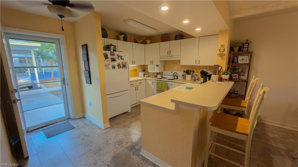 8298 Key Royal Lane, Unit 413 Naples, FL 34119 - Photo 11 of 18 Kitchen with light countertops, white appliances, a kitchen breakfast bar, a peninsula, and white cabinetry
