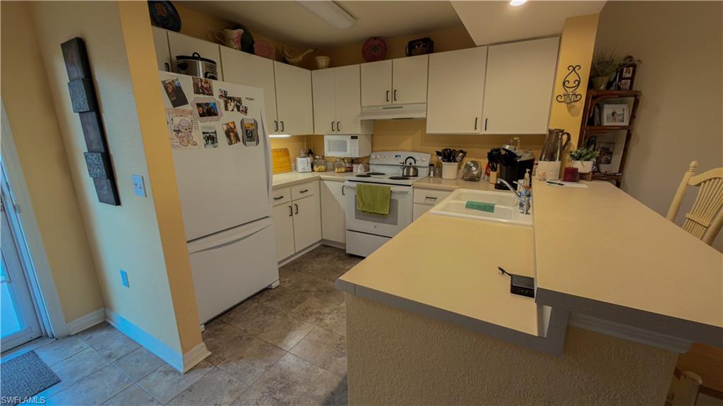 8298 Key Royal Lane, Unit 413 Naples, FL 34119 - Photo 2 of 18 Kitchen with light countertops, white appliances, a peninsula, and a breakfast bar area