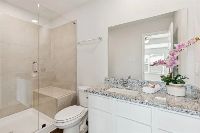 a bathroom with a granite countertop sink a toilet a mirror and shower