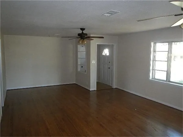 an empty room with wooden floor chandelier fan and windows