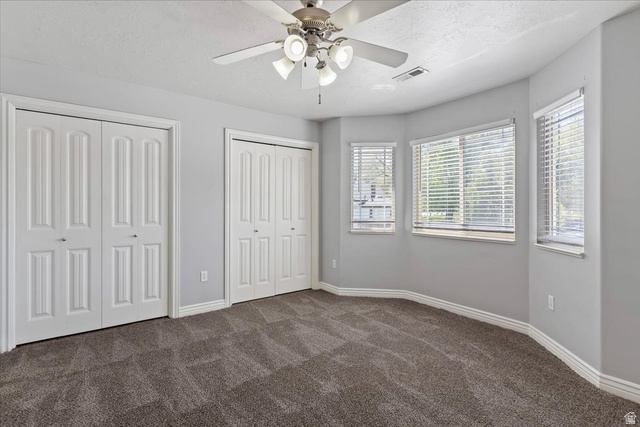 2350 South Highway 89, Unit 4 Perry, UT 84302 - Photo 25 of 30 Unfurnished bedroom with multiple closets, dark colored carpet, a textured ceiling, and a ceiling fan