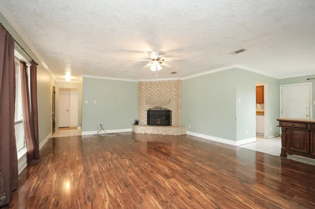 a view of an empty room with wooden floor and a fireplace