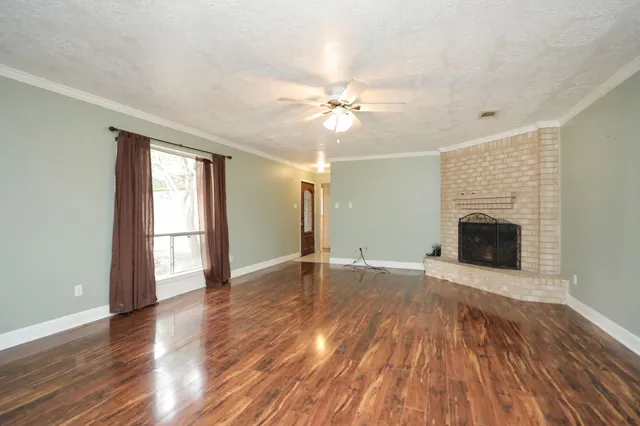 a view of an empty room with wooden floor fireplace and a window
