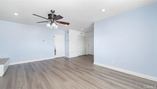 a view of an empty room with wooden floor and a ceiling fan