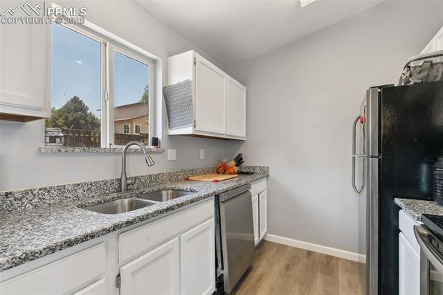 609 Wheat Field Road Fountain, CO 80817 - Photo 13 of 29 Kitchen with appliances with stainless steel finishes, light wood-style floors, white cabinets, and light stone countertops