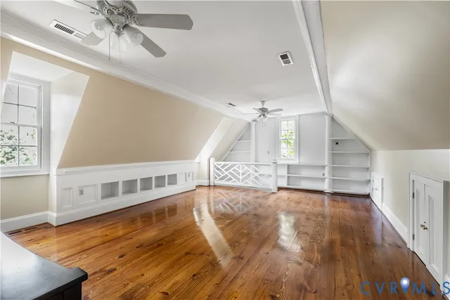 a view of an empty room with wooden floor and a ceiling fan