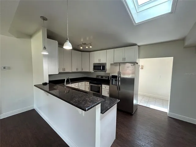 a kitchen with granite countertop a refrigerator a sink and white cabinets