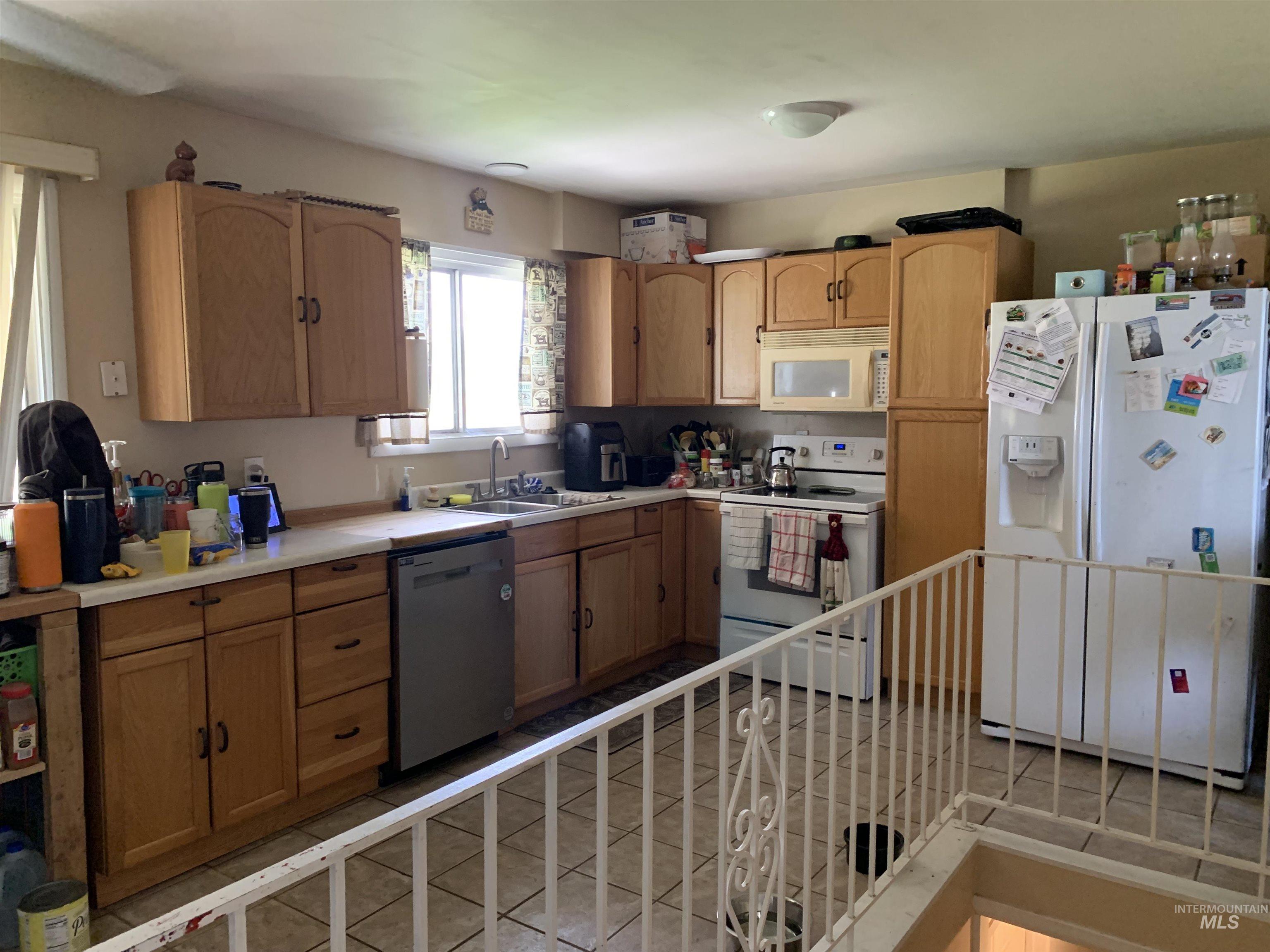 917 15th Drive Rupert, ID 83350 - Photo 3 of 4 Kitchen featuring wood cabinetry, light-toned countertops, tile flooring, and integrated white appliances including a range, microwave, and refrigerator