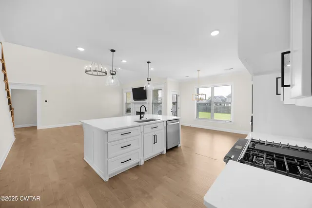 a kitchen with stainless steel appliances a sink wooden floor and white cabinets