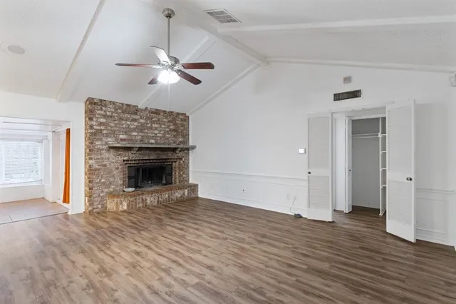 a view of an empty room with wooden floor fireplace and a window