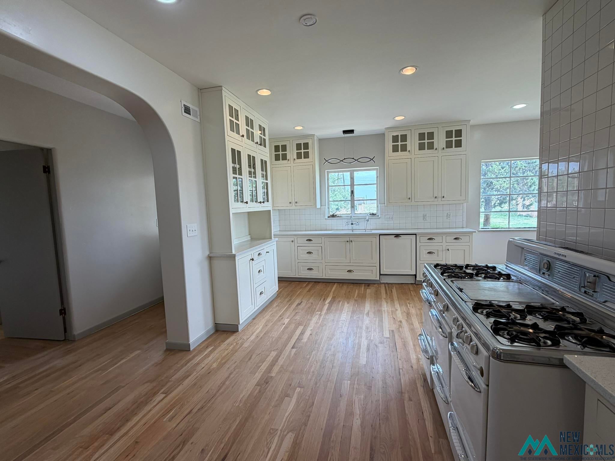 570 Curry Road North Clovis, NM 88101 - Photo 3 of 59 Spacious kitchen with wood-finish flooring, recessed lighting, white cabinetry with glass-front uppers, subway tile backsplash, and a large vintage-style range