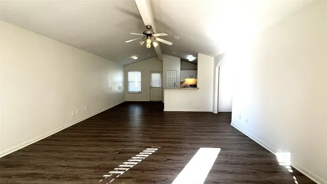 a view of an empty room with wooden floor and a ceiling fan