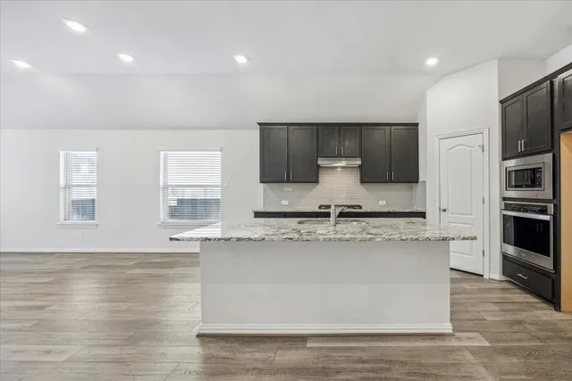 a large kitchen with stainless steel appliances a large counter top a stove and a wooden floors