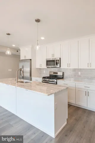 a kitchen with stainless steel appliances granite countertop a sink a stove a refrigerator and white cabinets