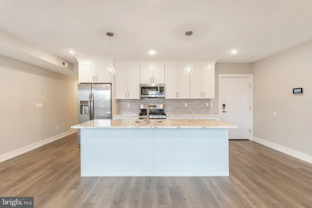 a view of kitchen with stainless steel appliances granite countertop a stove a sink a refrigerator and white cabinets with wooden floor