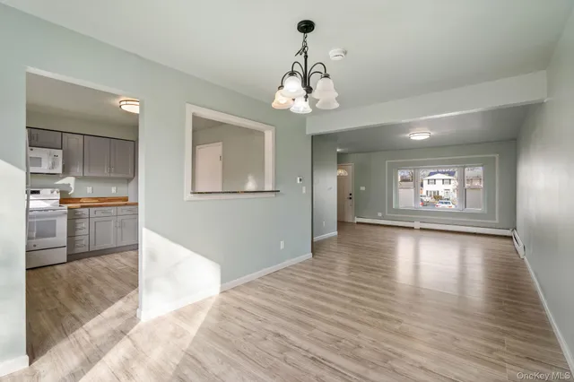 a view of an empty room with wooden floor and a kitchen