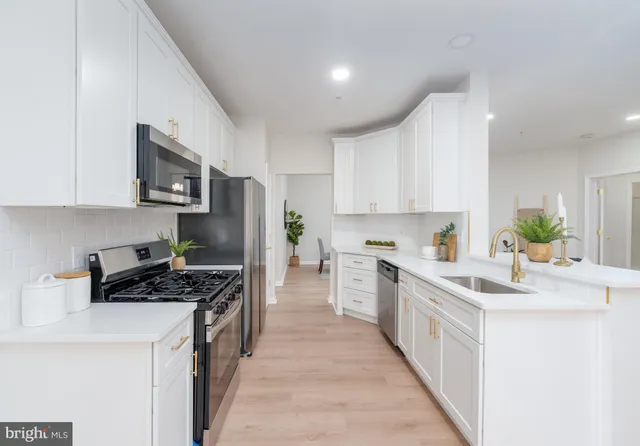 a kitchen with stainless steel appliances a stove a sink a refrigerator a stove top oven and white cabinets