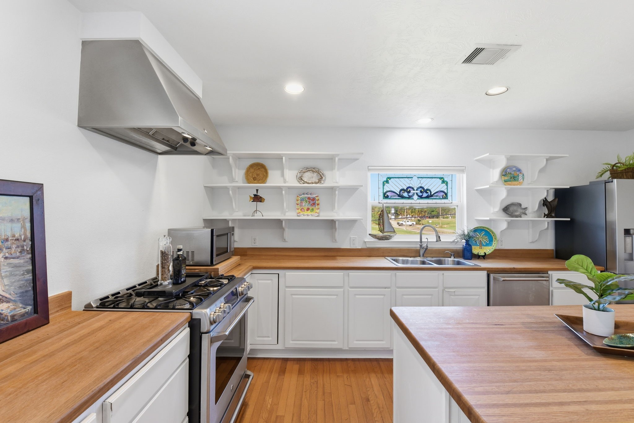 180 Grove Road Kemah, TX 77565 - Photo 13 of 30 This inviting kitchen boasts a bright, airy atmosphere with sleek stainless steel appliances, open shelving, and a charming stained glass.