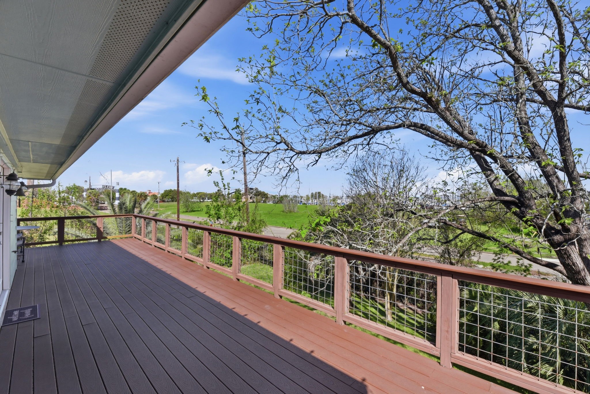 180 Grove Road Kemah, TX 77565 - Photo 28 of 30 This photo showcases a spacious deck with wood flooring and a wire railing, offering expansive views of lush greenery and a clear blue sky. It's a perfect space for outdoor relaxation and enjoying the natural surroundings.