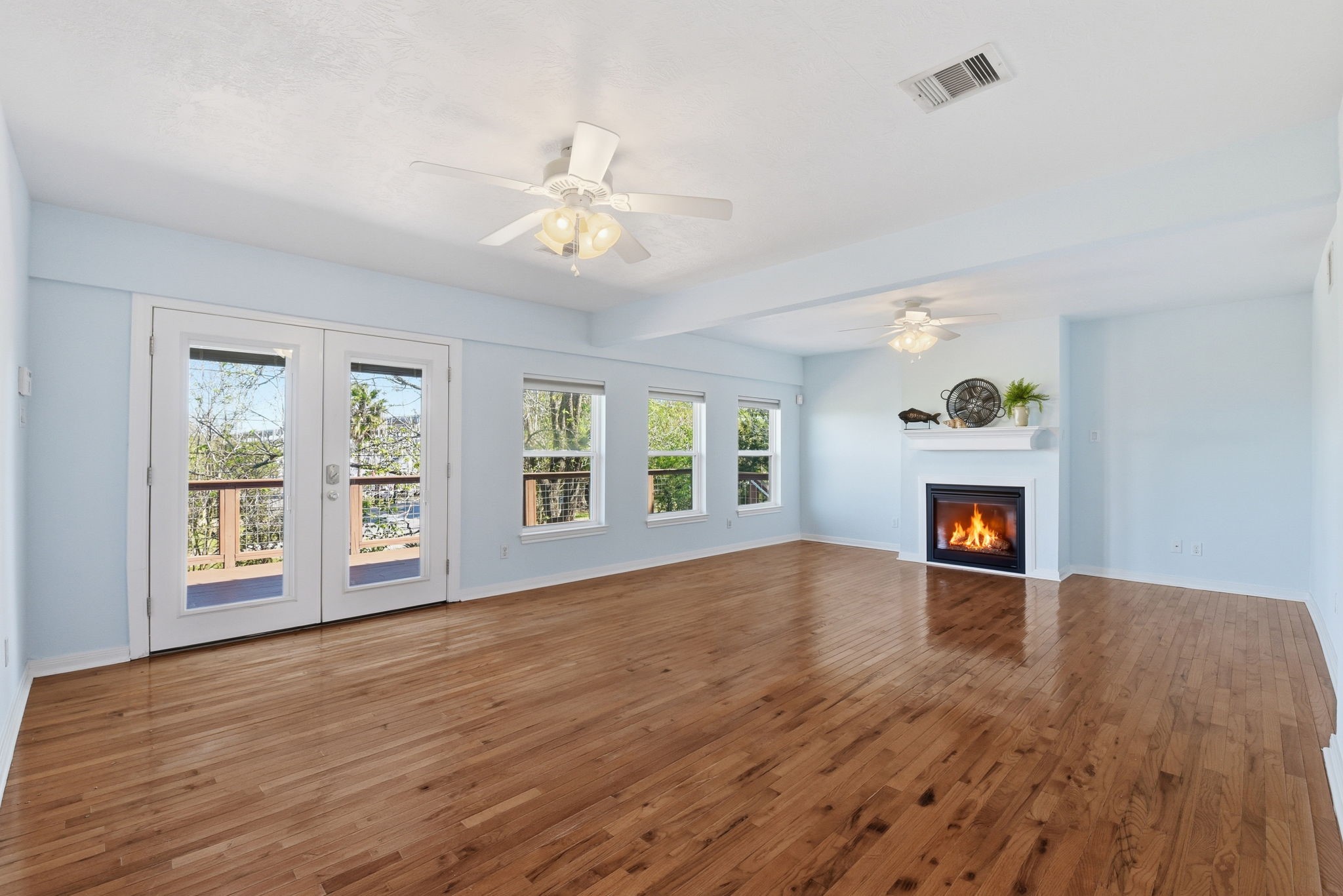 180 Grove Road Kemah, TX 77565 - Photo 9 of 30 This spacious living room, bathed in natural light from elegant French doors, features a cozy gas fireplace at the far end, perfect for relaxing evenings.